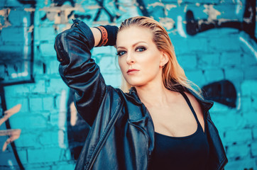 Obraz premium beautiful young blond woman in a black body in leather jacket standing on the background of painted wall on the street