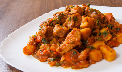 Stewed meat with vegetables in a plate on wooden table