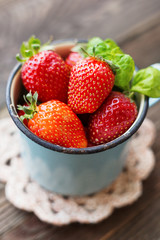 Fresh juicy strawberries  in old rusty mug. Rustic wooden background with crochet napkin.
