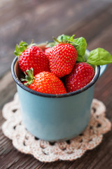 Fresh juicy strawberries  in old rusty mug. Rustic wooden background with crochet napkin.
