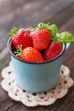 Fresh juicy strawberries  in old rusty mug. Rustic wooden background with crochet napkin.