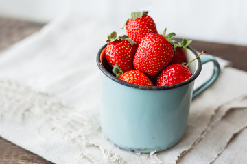 Fresh juicy strawberries  in old rusty mug. Rustic wooden background with homespun napkin.