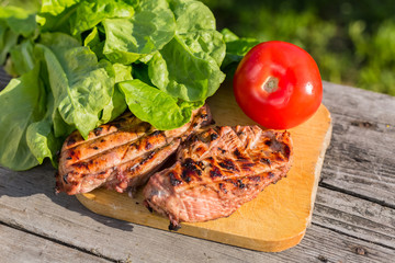 Two grilled chicken Breasts and red tomato with lettuce on wooden cutting Board on old wooden table on green background