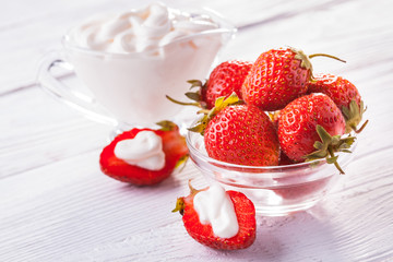 Fresh red strawberries with cream on the white wooden table.