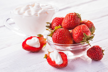 Fresh red strawberries with cream on the white wooden table.