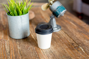 paper Cup of coffee on a wooden table next to a pot of green grass and light grey background on the sofa