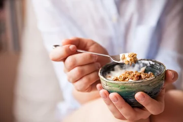 Poster Young woman with muesli bowl. Girl eating breakfast cereals with nuts, pumpkin seeds, oats and yogurt in bowl. Girl holding homemade granola. Healthy snack or breakfst in the morning.. © goodmoments