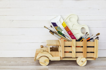 Toy wooden truck carries paint, brushes and palette on white pla