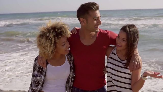 Young man embracing two attractive women on the beach and is under discussion.