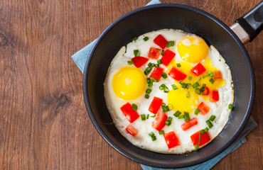 fried eggs with vegetables in a frying pan on wooden table