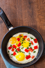 fried eggs with vegetables in a frying pan on wooden table