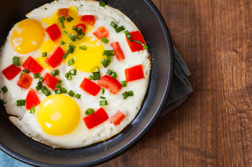 fried eggs with vegetables in a frying pan on wooden table