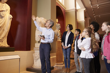 Pupils And Teacher On School Field Trip To Museum With Guide - obrazy, fototapety, plakaty