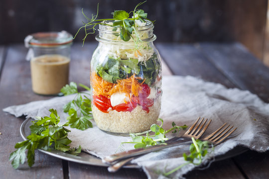 Rainbow salad in a jar, quinoa, tomatoes, mozzarella, spinach, pea sprouts, dressing aside