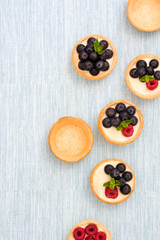 Delicious tartlets with raspberries and blueberries on blue background
