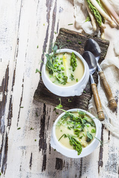 Cream of white asparagus soup garnished with white and green asparagus spears, pea shots and chives
