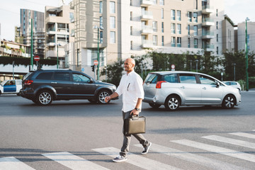 Young handsome business man holding briefcase walking on pedestrian crossing  outdoor in the city, looking over smiling - business, work, happiness concept