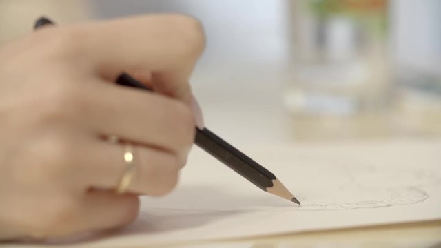 The girl draws pencil sketch on paper. Close-up slow motion footage.