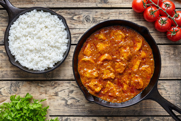 Chicken tikka masala traditional Asian spicy meat food with rice tomatoes and parsley in cast iron pan on vintage wooden background