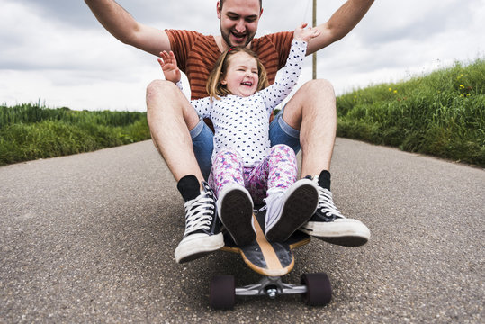 Daughter and father sitting on skateboard