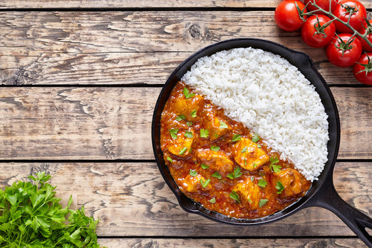Chicken tikka masala Asian traditional spicy meat food and rice in cast iron skillet with tomatoes, butter and parsley on vintage wooden background