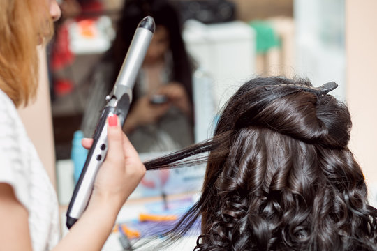 Stylist in barber salon using curling iron for brunette hair curls, close-up