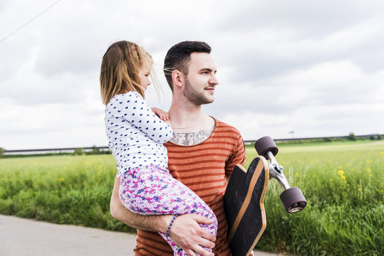 Father with skateboard holding daughter