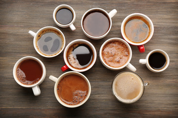 Different cups of coffee on wooden table, top view