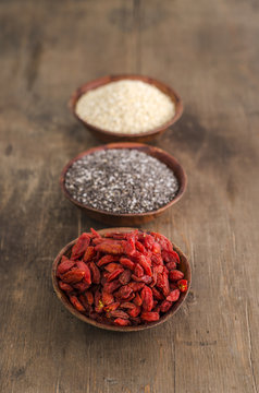 Three wooden bowls of dried wolfberries, chia and quinoa