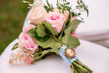 fresh and beautiful wedding bouquet with cameo on a white chair