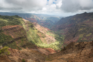 Sunlight on the Waimea Canyon floor. The canyon floor is in the sun while the sides are in the shadow. The rain in a distance washes out the colors of distant objects.