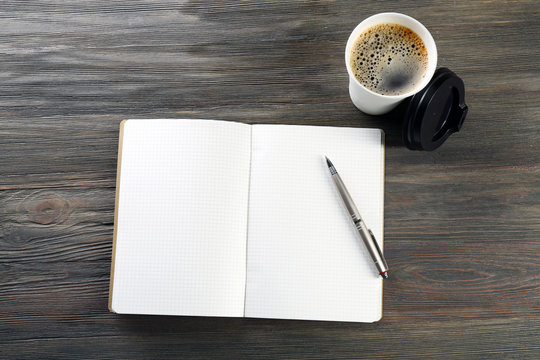 Cup of fresh coffee and notebook on wooden background