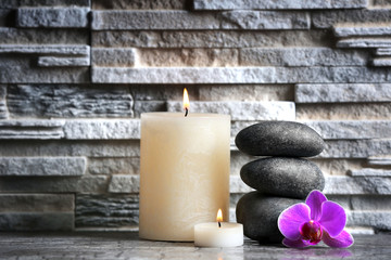 Fototapeta na wymiar Composition of spa pebbles, flowers and candles on grey brick wall background
