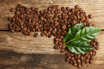 Coffee beans and green leaves on wooden background