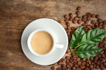 Cup of coffee with beans and leaves on wooden background