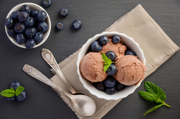 Fototapeta na wymiar Chocolate ice cream with blueberries in white bowl on black slate background, top view
