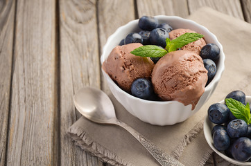 Chocolate ice cream with blueberries in white bowl on rustic wooden background, selective focus, horizontal permission, copy space