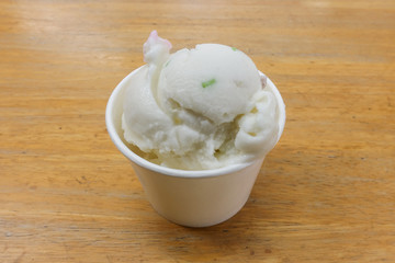 Homemade coconut icecream in paper cup on the wooden table.