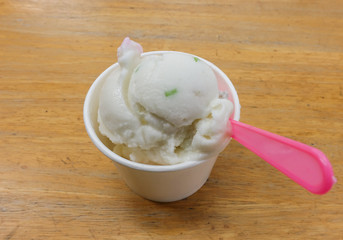 Homemade coconut icecream in paper cup with pink plastic spoon o