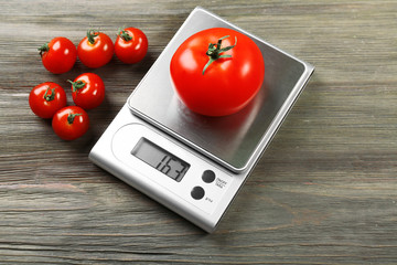 Tomatoes with digital kitchen scales on wooden background