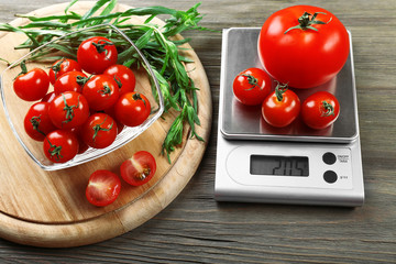 Tomatoes with digital kitchen scales on wooden background