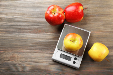 Apples with digital kitchen scales on wooden background