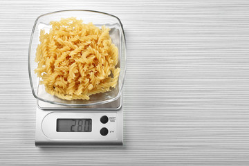 Pasta with digital kitchen scales on wooden background