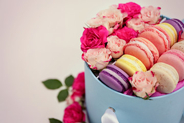 Tasty macaroons and roses in box on light background