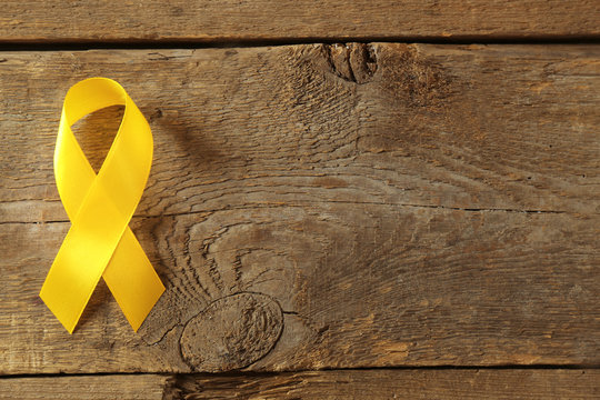 Yellow awareness ribbon on wooden background