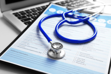 Stethoscope with medical form and laptop, close-up