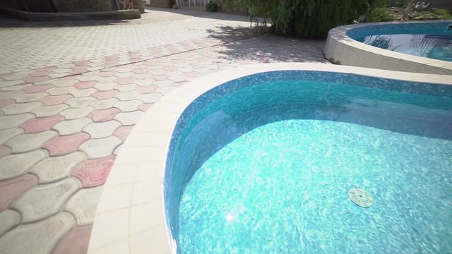 Camera moves along private swimming pool with paved deck at vacation home steadicam shot