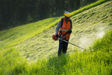 The worker in a uniform and mask cuts off a grass