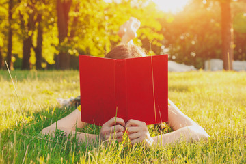 girl reading book lying in warm summer grass