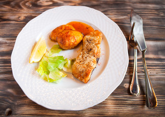 Grilled fish with potatoes, slice of lemon and red sause on wood